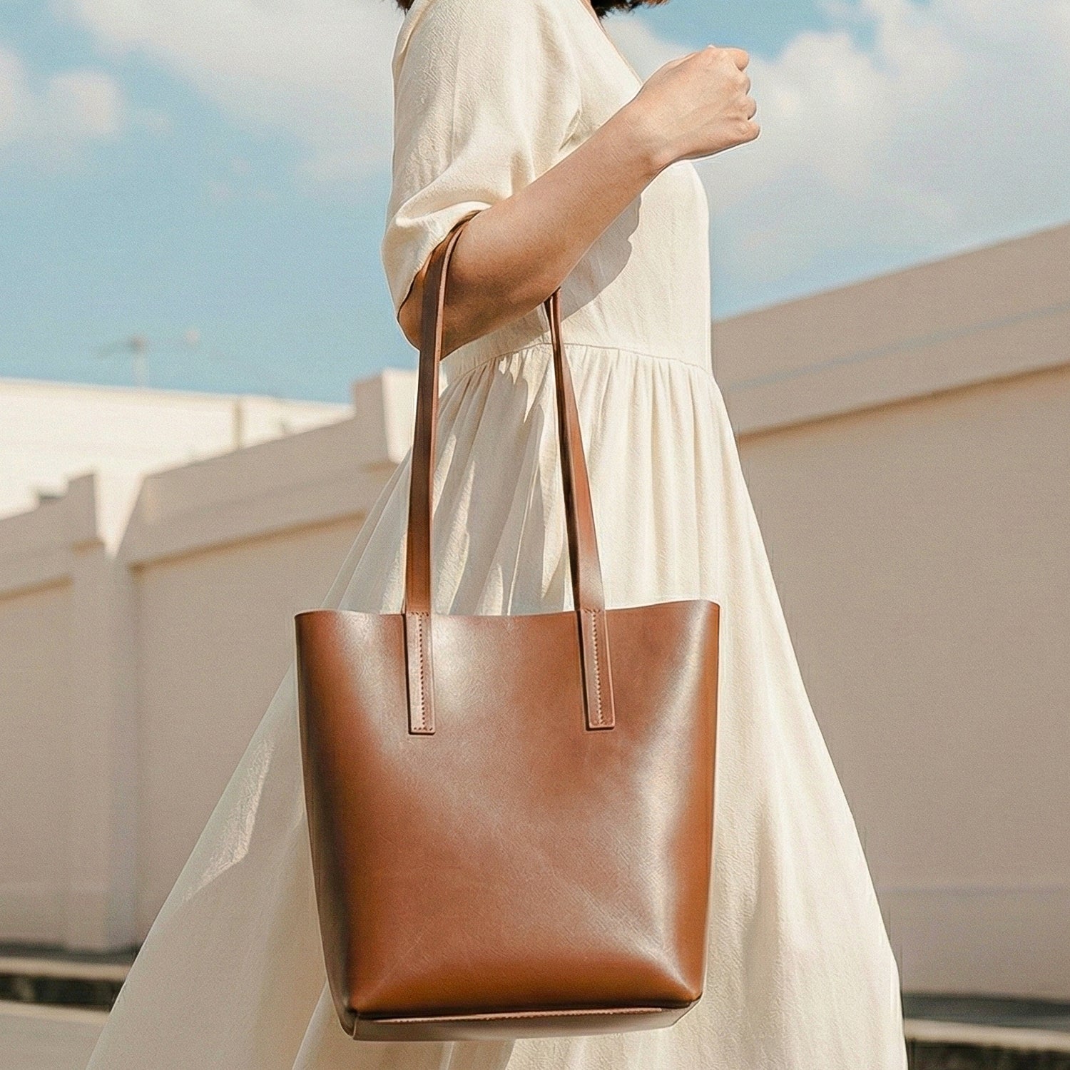 Person holding a brown leather tote bag with a light background