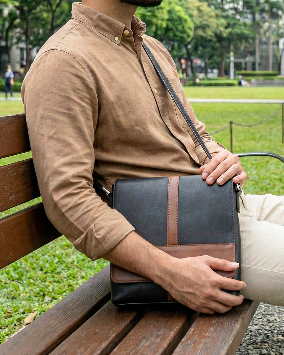 Person sitting on a park bench holding a black leather clutch bag.