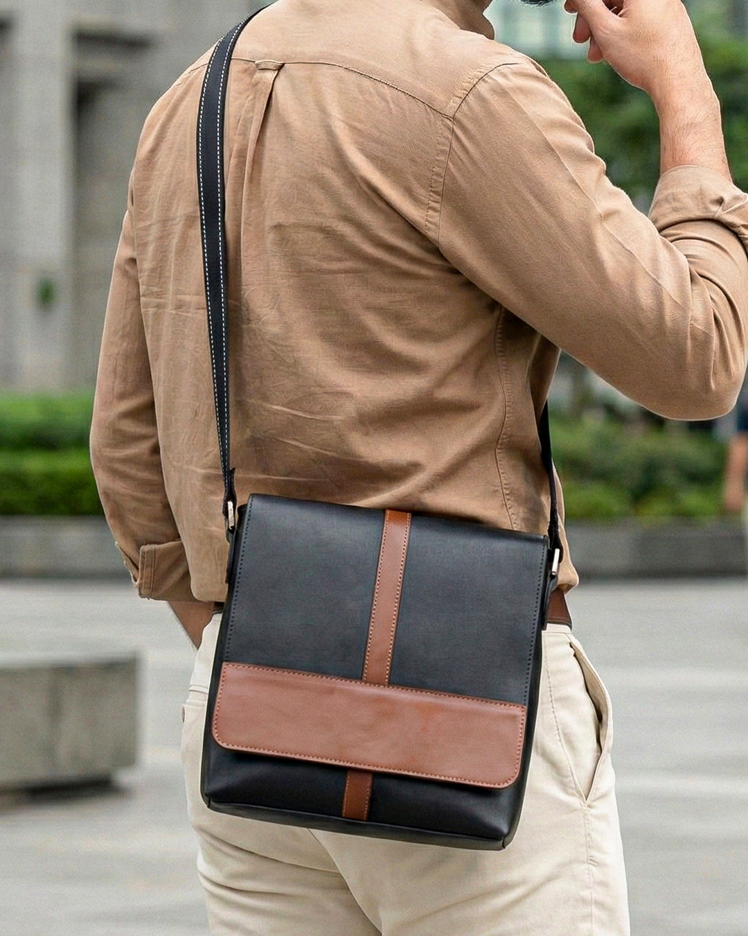 Man wearing a black and brown leather crossbody bag outdoors.
